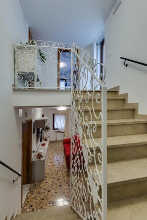 A staircase with a white metal railing, a red chair, and a tiled floor. - San Marco (Venice)