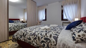 Ett hotellrum med en stor säng, en spegel och två fönster med tunna, genomskinliga gardiner.