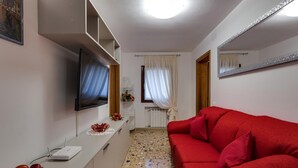Ett modernt vardagsrum med en röd soffa, en platt-TV som är monterad på väggen, ett vitt avlastningsbord och ett klinkergolv.