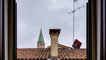 A view through a window of a building with a tiled roof, a chimney, and a tower with a green roof.