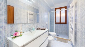 Um banheiro com pia branca, espelho, chuveiro e vaso sanitário.