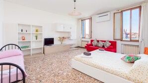 Quarto de hotel moderno com uma cama, um sofá vermelho, uma TV e vista para a cidade.