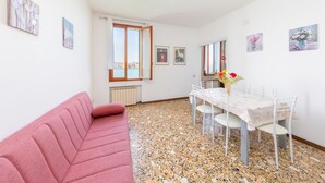 Quarto com um sofá vermelho, uma mesa de jantar com cadeiras e vista da cidade por grandes janelas.