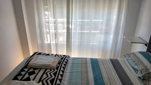 Ett hotellrum med en säng, ett fönster med tunna gardiner och ett nattduksbord.