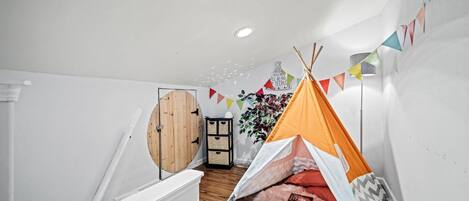 A cozy room with a wooden door, a small bookshelf, a tent, and a plant.