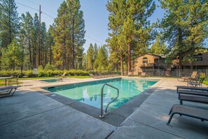 A rectangular swimming pool with a metal ladder, surrounded by lounge chairs and benches, with tall trees and a building in the background. - Fantastic Updated Family Condo, A/C, Next to Seasonal Pool & Hot Tub, Forest Views, Close 2 Golf (Sunriver)