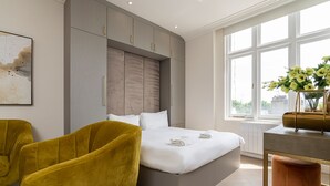 Een moderne slaapkamer met een groot bed, een gele fauteuil en stadszicht door een groot raam.