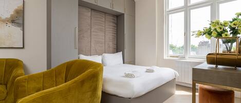 A modern bedroom with a large bed, a yellow armchair, and a view of the city through a large window.