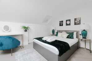 A modern bedroom with a bed, bedside tables, a desk, a chair, and a potted plant.
