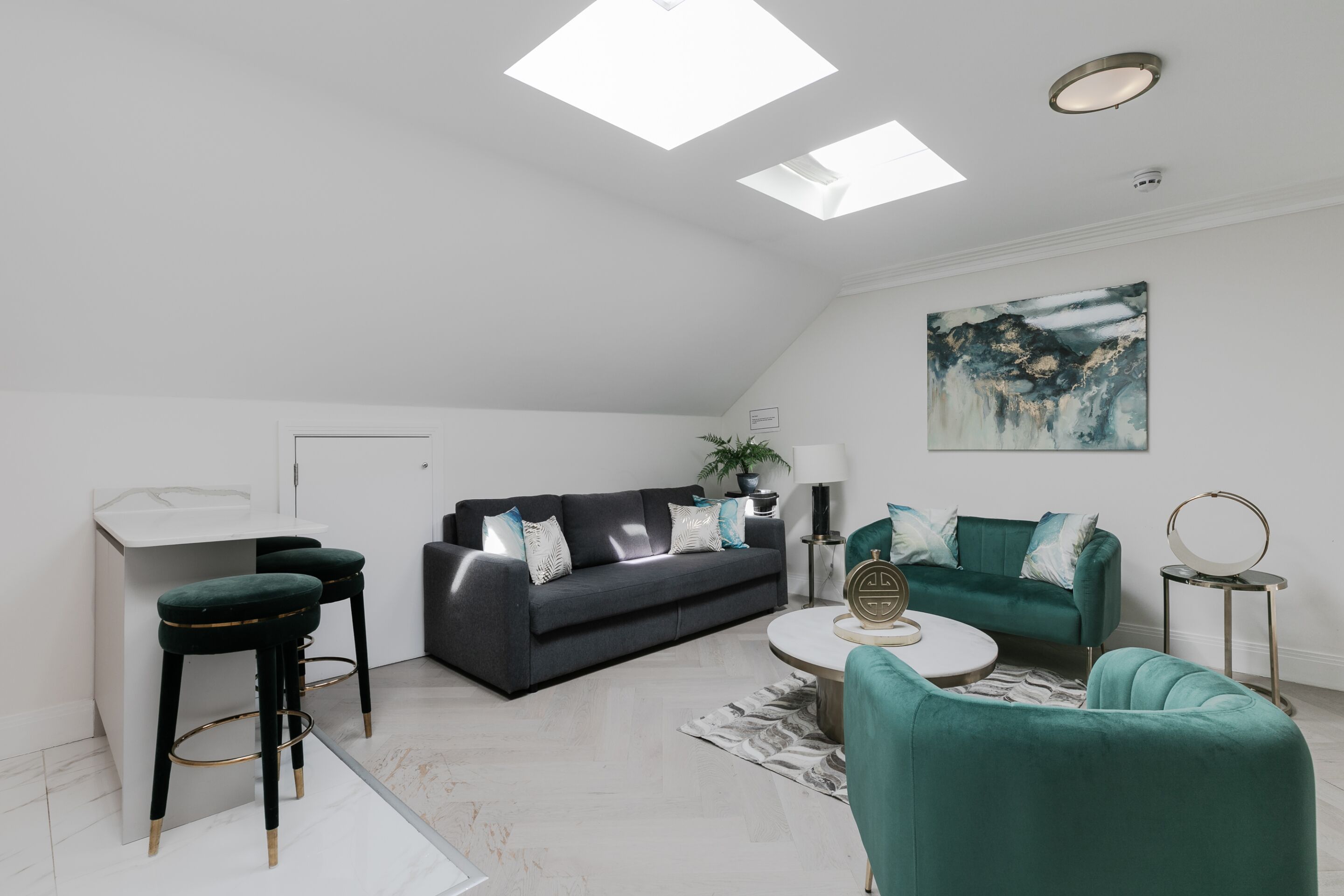 A modern living room with a dark grey sofa, teal armchairs, a white coffee table, and a painting on the wall.
