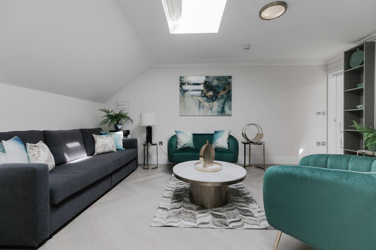 Ein modernes Wohnzimmer mit einem grauen Sofa, einem türkisfarbenen Sessel und einem runden Couchtisch.