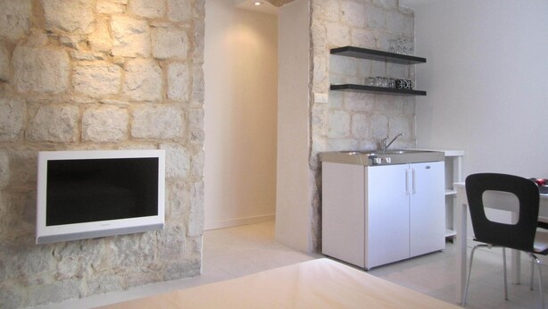 A compact kitchen with a stone wall, a built-in TV, and a dining area with a chair. - Eco B&B Old Town Beach (Split)