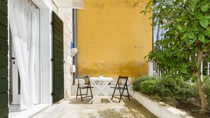 A small outdoor patio with a table and chairs, a yellow wall, and a tree. - Eco B&B Old Town Beach (Split)