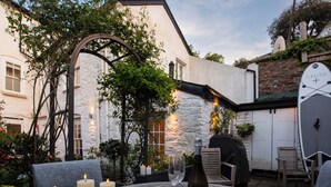 Eine Terrasse im Freien mit einem Tisch, gedeckt für eine Mahlzeit, umgeben von Kerzen und einer Weinflasche.