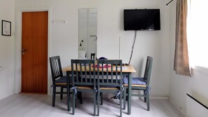 A dining area with a wooden table and four chairs, a flat-screen TV mounted on the wall, and a door to the left. - Hovstø (Seljord)