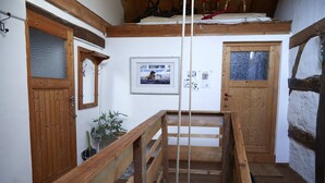 Una escalera de madera con barandilla de cuerda, puertas de madera con paneles de vidrio y un cuadro en la pared.