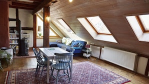 Acogedor dormitorio en ático con una mesa de comedor, sillas y un tapete estampado. Hay tragaluces, una estantería y un radiador.