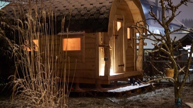 Una cabaña de madera con techo inclinado, un porche pequeño y una ventana.