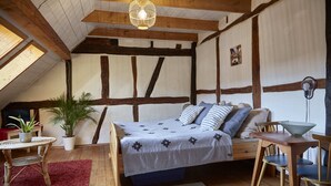 Un dormitorio acogedor en el ático con vigas de madera a la vista, una cama grande con ropa de cama estampada, una mesa de comedor con sillas y una planta en maceta.