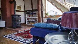Una habitación acogedora con techo de madera, un sofá con cojines a rayas, una estantería y un tapete rojo con estampado.