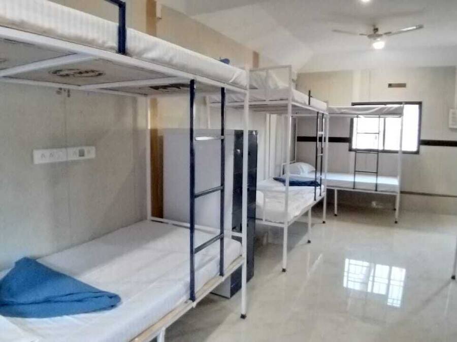 A dormitory room with bunk beds, a ceiling fan, and a window providing natural light.