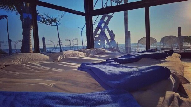 Una cama con vista a la playa y al océano a través de amplias ventanas.