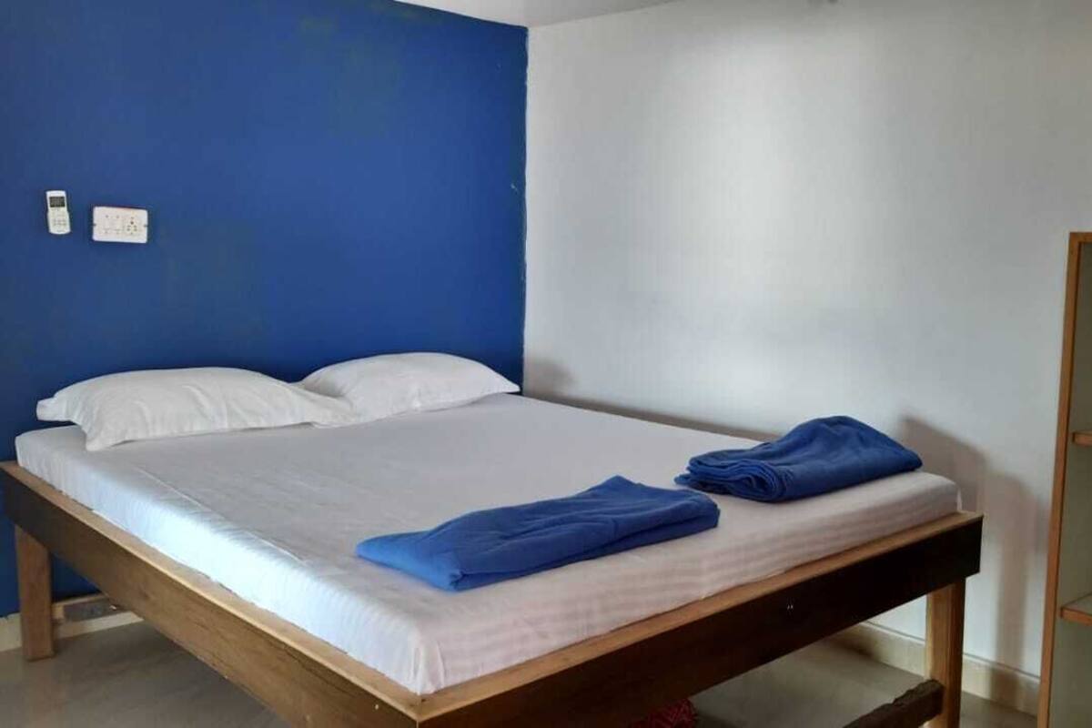 Una cama individual con ropa de cama blanca y toallas azules, un cabecero de madera y una pared blanca con un detalle en azul.