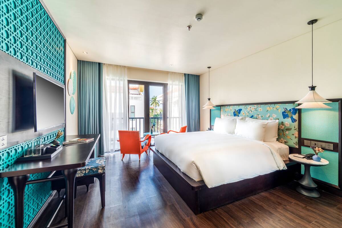 A hotel room with a large bed, a desk with a computer, a chair, and a TV.