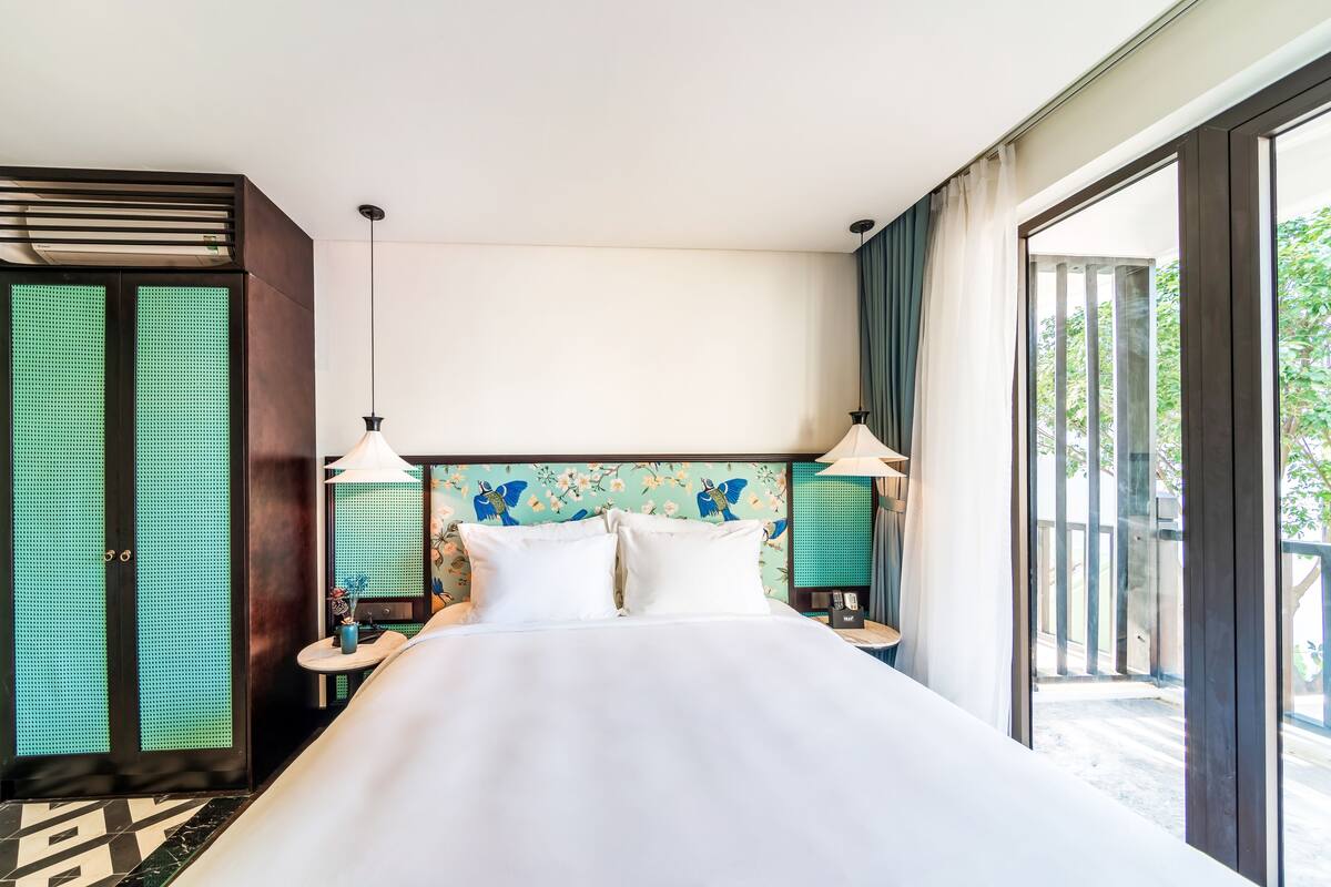 A hotel room with a large bed, two bedside tables with lamps, a decorative headboard, and a sliding glass door to the outside.