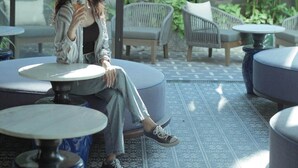 A woman sitting at a table in a cafe with large windows and hanging pink paper lanterns. - De An Hotel (Da Nang)
