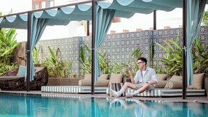 A poolside area with a sofa, striped cushions, and a wicker chair. - De An Hotel (Da Nang)
