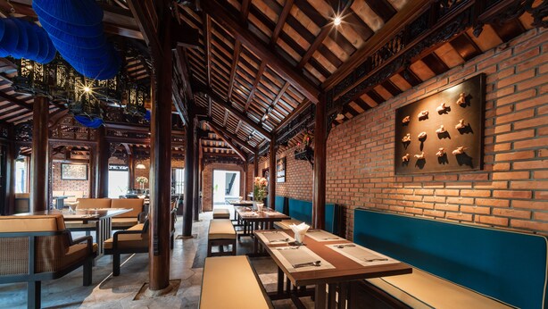 A restaurant with brick walls, wooden beams, and blue hanging decorations. - De An Hotel (Da Nang)