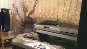Una stanza con pavimento in legno, vasca idromassaggio, una sedia di legno e una parete con motivo decorativo.