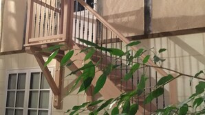 Una scala in legno con ringhiera che conduce a una porta con finestre. In primo piano, una pianta.