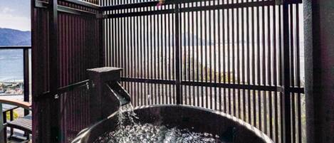 A hot tub with water flowing from a faucet, enclosed by a metal fence with a view of the sea in the background.