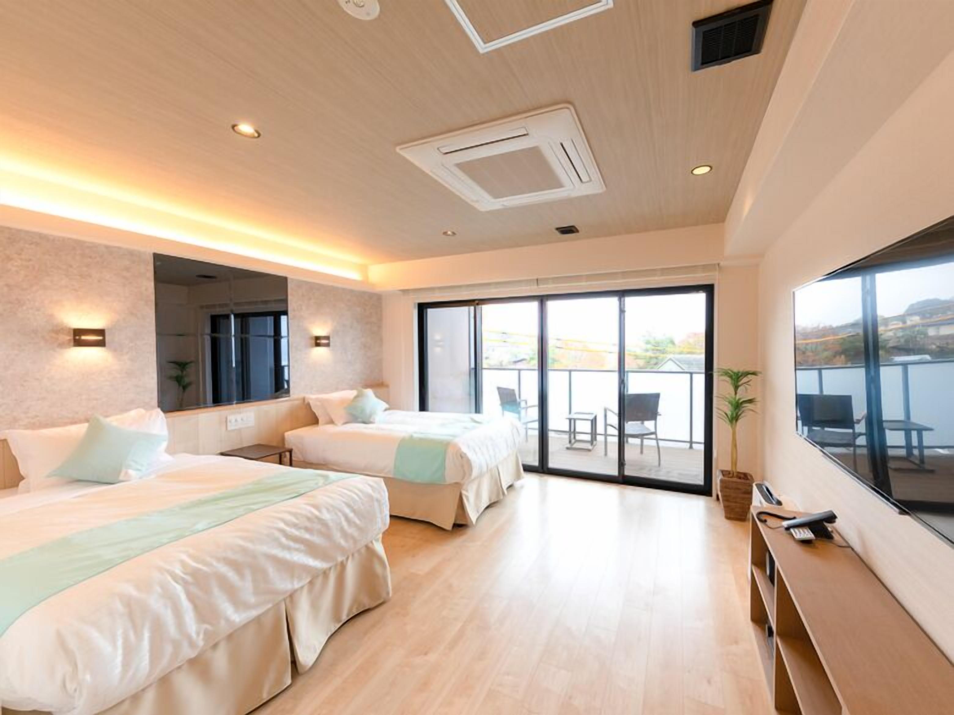 A modern hotel room with two beds, a balcony, and a large window.