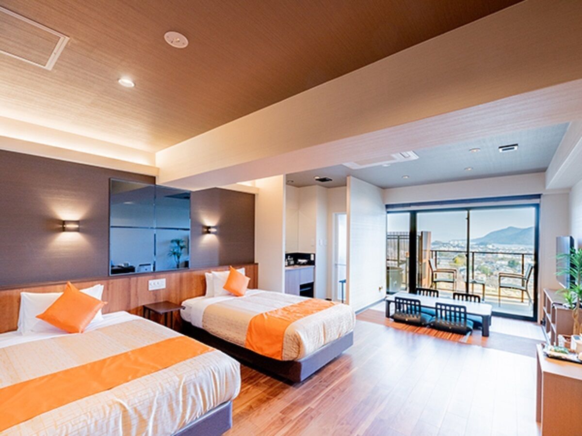 A modern hotel room with two beds, a balcony with a view, and a dining area.