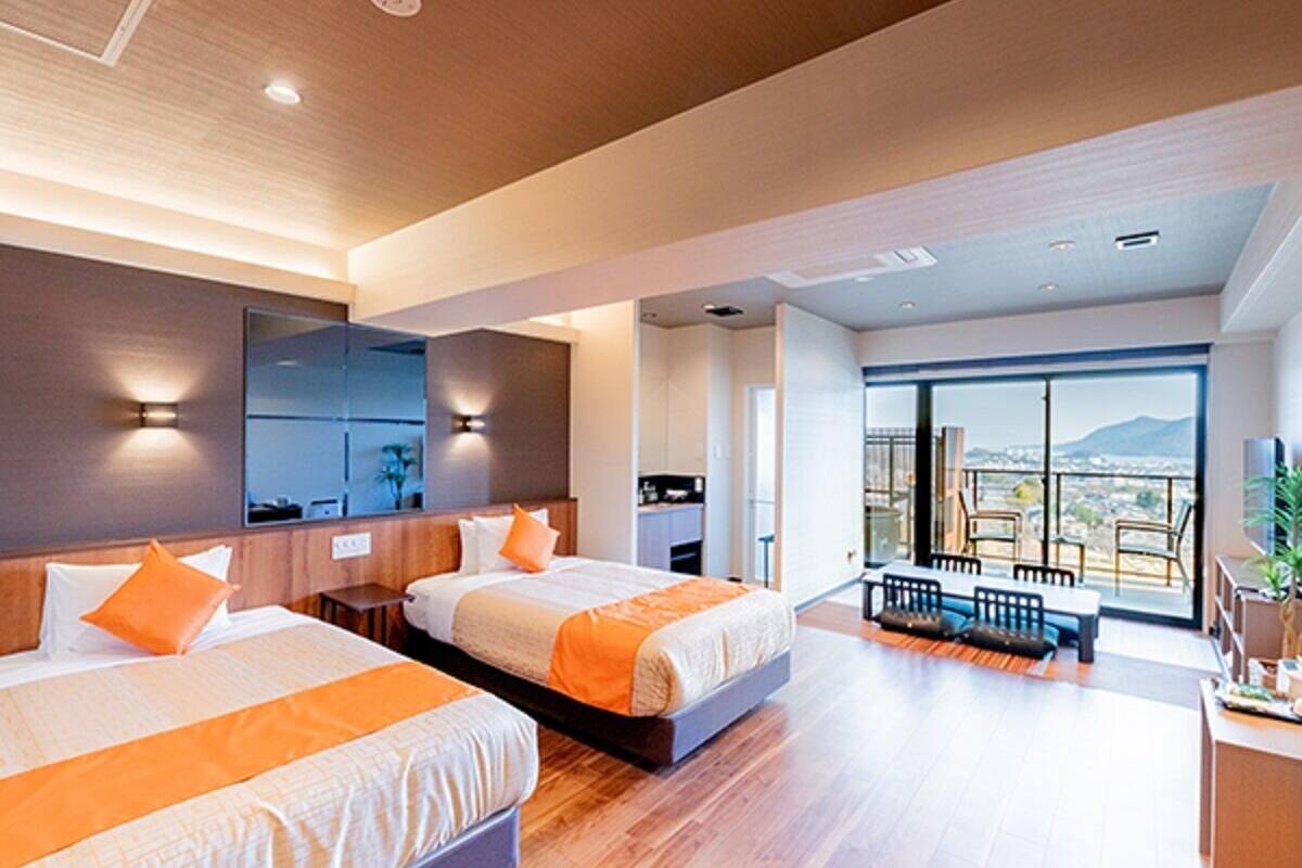 A modern hotel room with two beds, a balcony with a view, and a dining area.