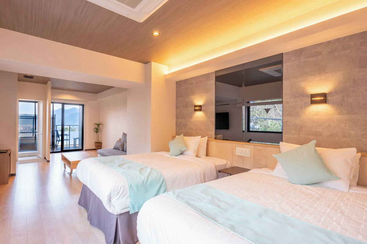 A modern hotel room with two beds, a large mirror, and a balcony with a view.