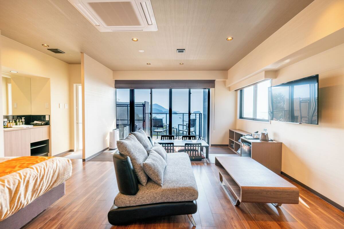 A modern hotel room with a sofa, a dining table, and a TV.