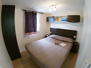 A bedroom with a bed, a nightstand, a wall-mounted TV, and a window with curtains.