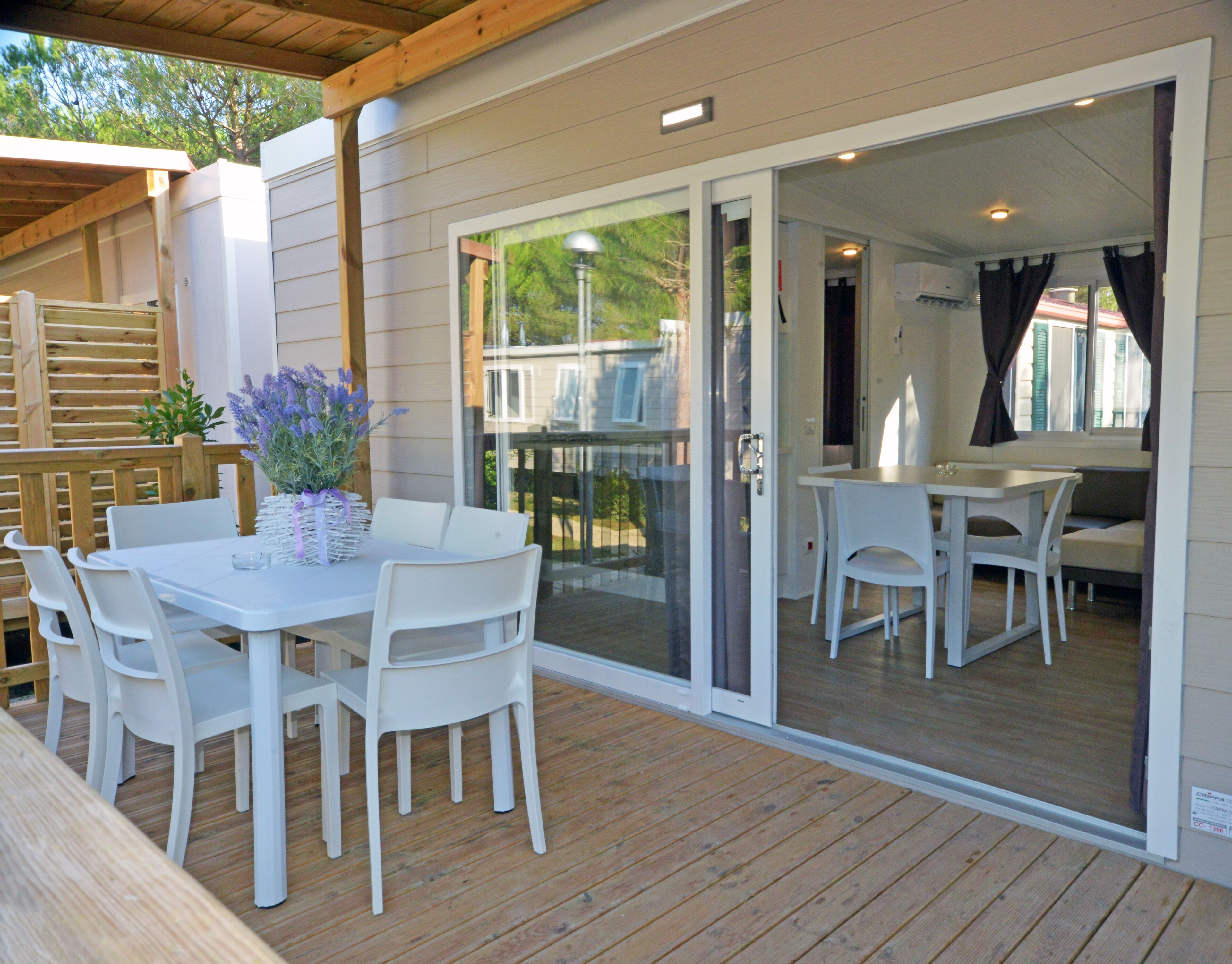 An outdoor patio with a table and chairs, a glass door leading to an interior space, and a wooden deck.