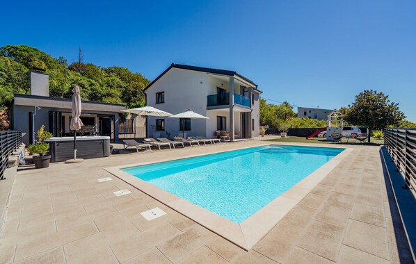 Ett modernt hus i två våningar med en swimmingpool, utomhusmöbler och en vattenrutschkana.