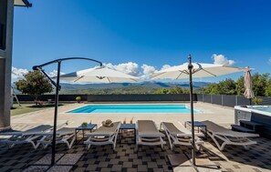 Ett poolområde med solstolar och parasoller, en pool och utsikt över bergen.