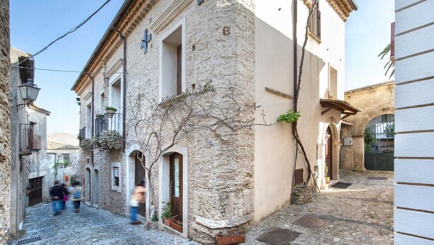 A narrow cobblestone street with historic buildings, including a stone wall with a cross and a building with a wooden door. - 4 bedroom beautiful home in Ciminà (Ciminà)