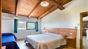 A bedroom with a wooden ceiling, a bed with a white quilt, a bedside table with a lamp, a window with green curtains, and a view of the outdoors. - 4 bedroom beautiful home in Ciminà (Ciminà)