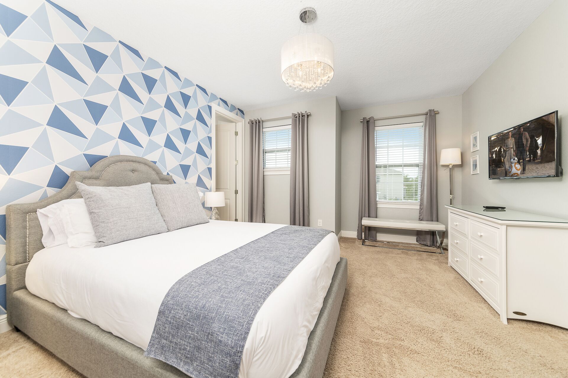A bedroom with a bed, a bench, a dresser, and a chandelier.