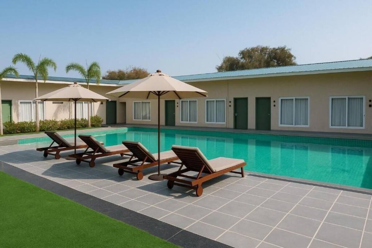 Un área junto a la piscina con sillones de descanso y sombrillas, una piscina y un edificio con techo verde.