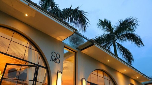 A hotel with arched windows, a visible 'COMO' sign, and palm trees in the background. - Status Club Resort (Kanpur)
