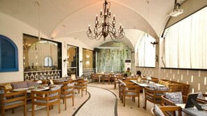 A spacious dining area with wooden furniture, a chandelier, and a view of the kitchen through a glass partition. - Status Club Resort (Kanpur)